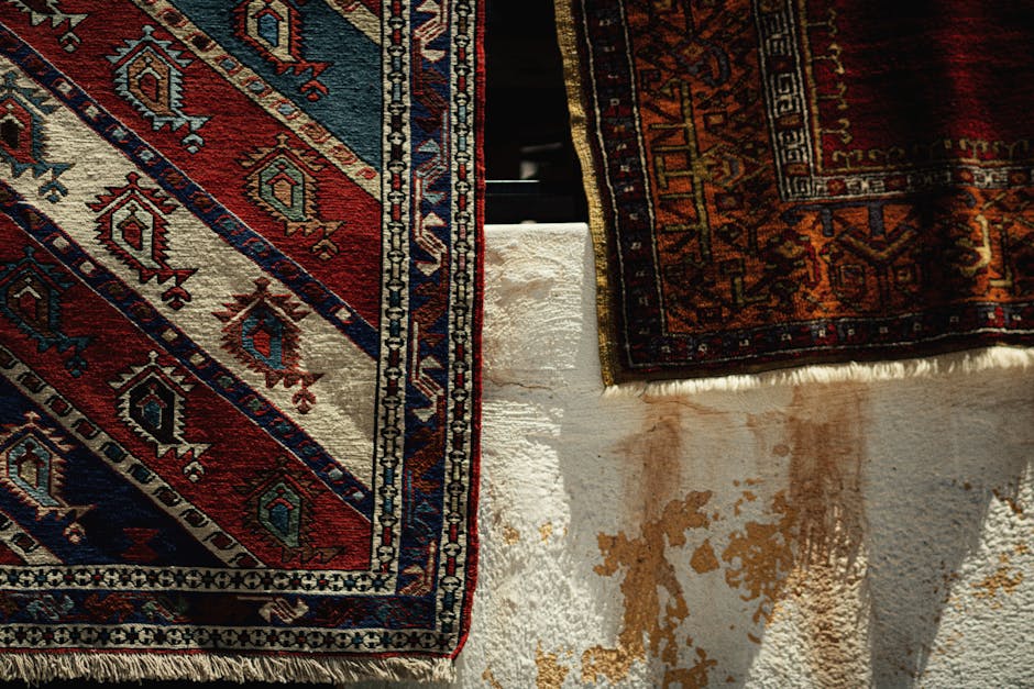 A close-up of a person vacuuming a patterned area rug with a modern, black vacuum cleaner in a well-lit room. The rug features intricate floral designs in soft pastel shades, and the vacuum's head is positioned on the surface, demonstrating surface cleaning. Behind the vacuum, a person wearing white shoes and dark trousers is partially visible, indicating a professional cleaning process. The room appears tidy and bright, emphasizing the thoroughness of the cleaning service provided by Knightsbridge Carpet Cleaners at Eaton Square in Knightsbridge.