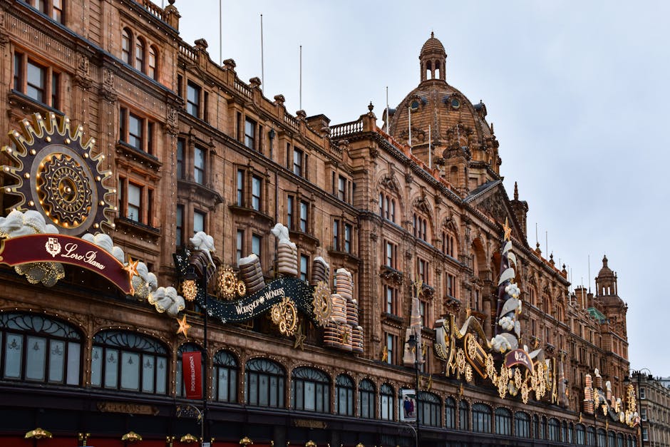 Exterior view of a historic building in Knightsbridge decorated with festive holiday ornaments, including large white cotton-like decorations, golden gears, stars, and chocolate-themed confectionery sculptures positioned along the upper facade. The building features elaborate architectural details with large arched windows on the ground floor and intricate stonework. Natural daylight illuminates the scene, highlighting the cleanliness and well-maintained appearance of the decorations, which evoke a festive atmosphere suitable for surface cleaning and thematic decoration maintenance by Knightsbridge Carpet Cleaners, as featured on the Knightsbridge carpet cleaning near Harrods Brompton Road guide webpage.